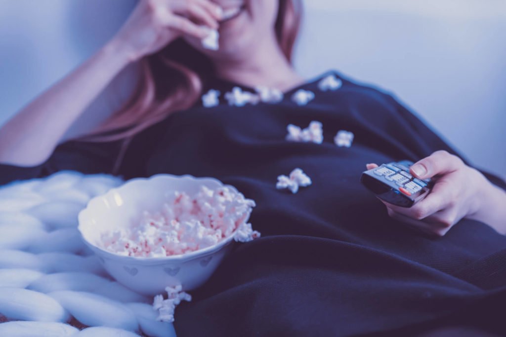 A girl watching Tv and eating popcorn