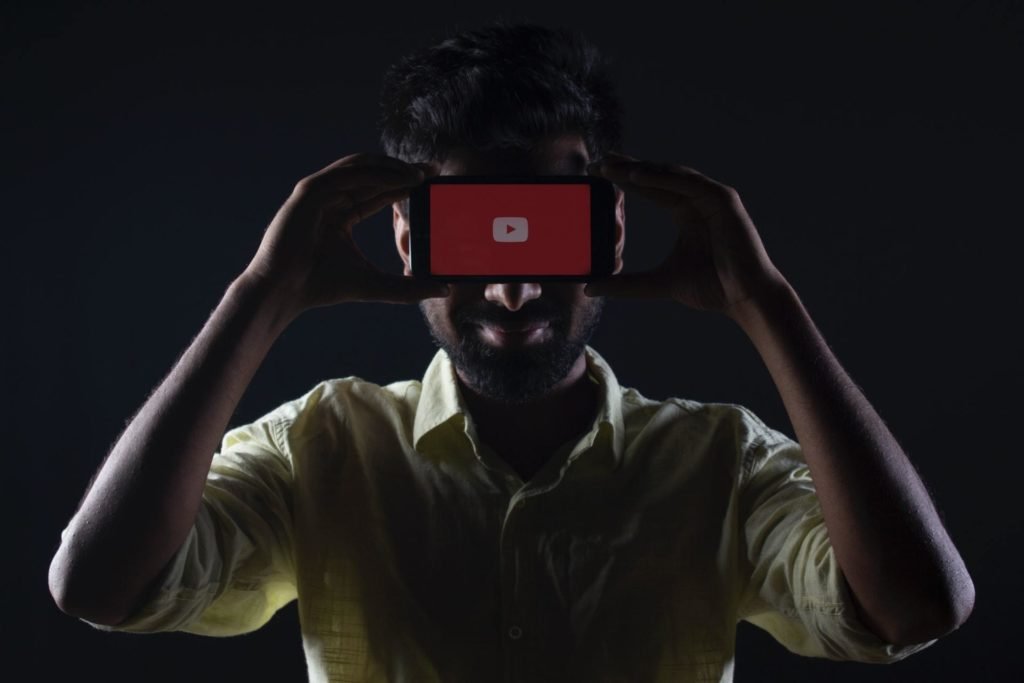 A man holding a phone above his eyes which says YouTube